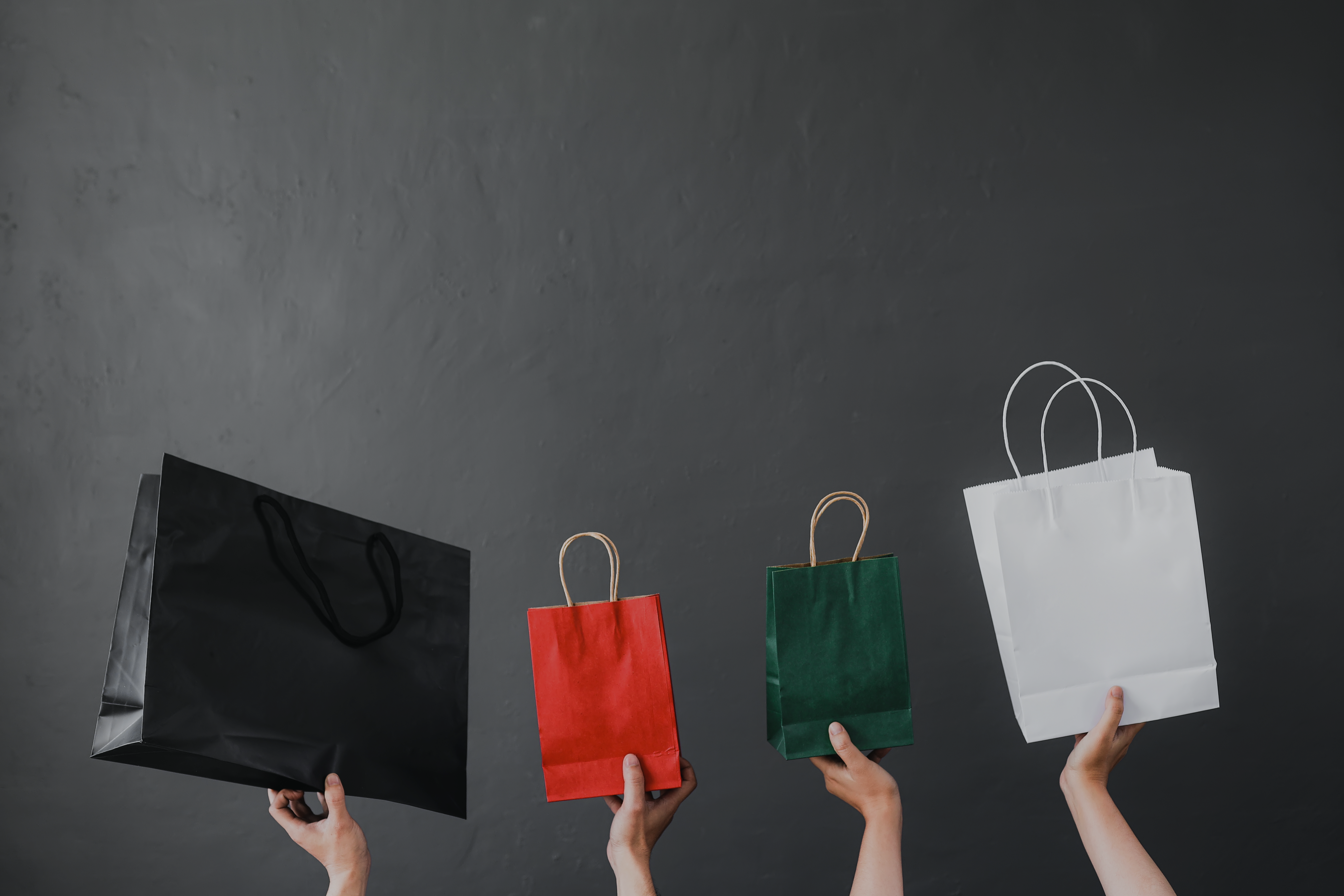 Ihmisten kädet pitelevät erivärisiä ostoskasseja mustaa taustaa vasten, symboloiden retail media -ratkaisujen mahdollisuuksia kaupan alalla.