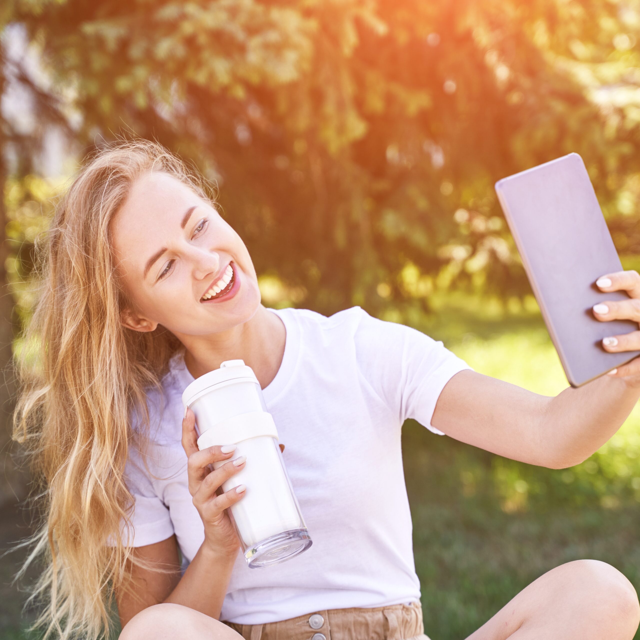 Nuori nainen ottaa ulkona ugc selfien termosmukin kanssa.